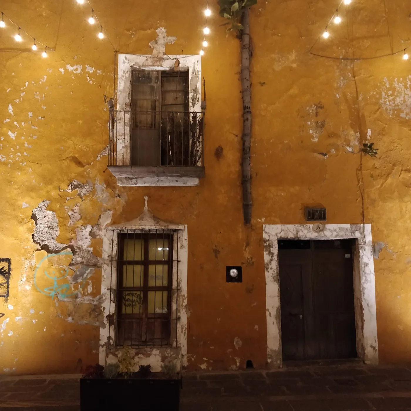 A weathered ochre colonial façade with wrought-iron balcony at dusk