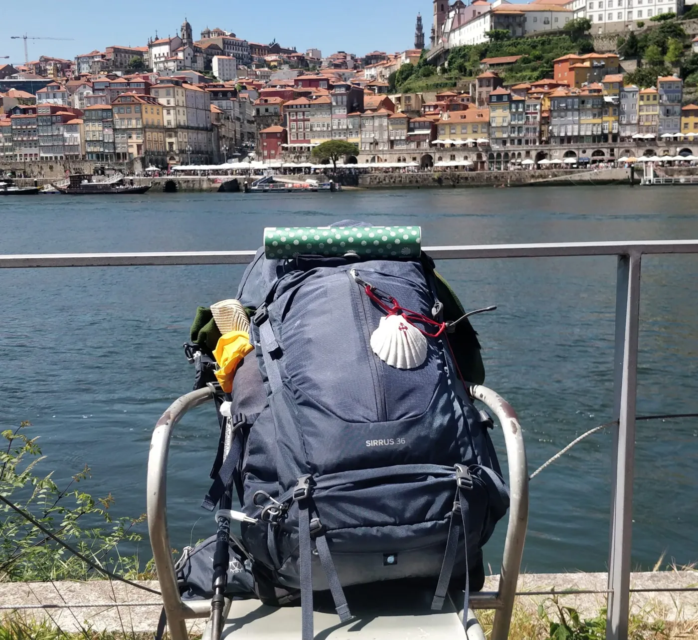 A backpack with a scallop shell resting by the river in Porto